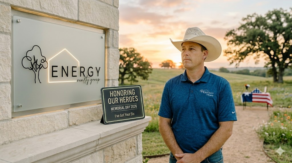 Respectful sunrise portrait of Marine Veteran and Real Estate Broker Nick Getzendanner in a cowboy hat leaning against a stone wall. He is looking off-camera. Behind him, the backlit ENERGY Realty Group logo (with tree/house line-art) from image_0.png is visible, along with a integrated digital display showing 'HONORING OUR HEROES' and 'Memorial Day 2026'. The background shows a gentle North Texas landscape in Parker or Tarrant County.