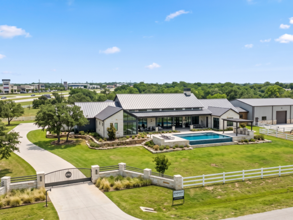 An aerial view of a luxury modern Texas Hill Country estate with a gated entry, private swimming pool, and detached custom workshop on acreage, positioned near the growing commercial corridor between Hudson Oaks and Weatherford.